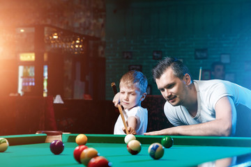 Father and son play billiards. The father teaches his son to play billiards. The concept of parents and children, upbringing, family rest.