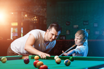 Father and son play billiards. The father teaches his son to play billiards. The concept of parents and children, upbringing, family rest.