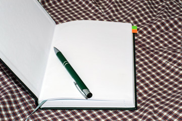open notebook black color and ballpoint pen green checkered background