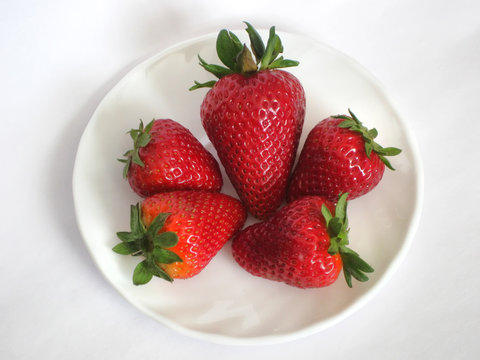 Five strawberries laying on white plate on white background.