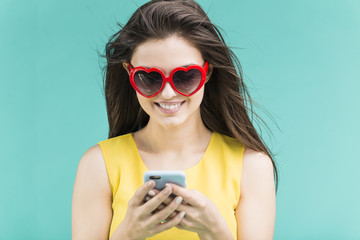 Beautiful smiling brunette girl wears yellow t-shirt and sunglasses texting happily by smartphone...
