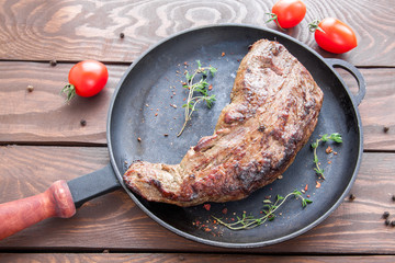 roast beef steak with crust sprinkled and spices and twigs of thyme on a black iron frying pan on a wooden table