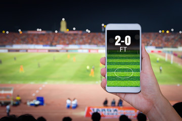 Hand holding smartphone with blur football field background.