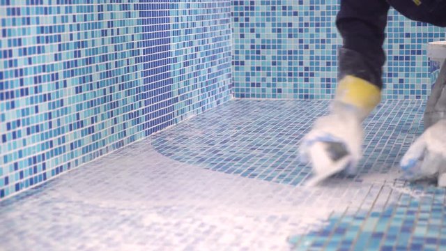 pool tile installation, laborer's hands installing blue swimming pool tile with trowel, tripod. 4 k