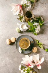 Obraz na płótnie Canvas Blue cup of black espresso coffee french dessert macaroons, cream and spring flowers magnolia, blooming cherry branches over grey texture background. Top view, space. Spring greeting card. Toned image