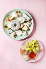 Cheese plate assortment of french cheese served with honey, walnuts, bread and grapes on turquoise ceramic plate over pink pastel background. Top view, space.