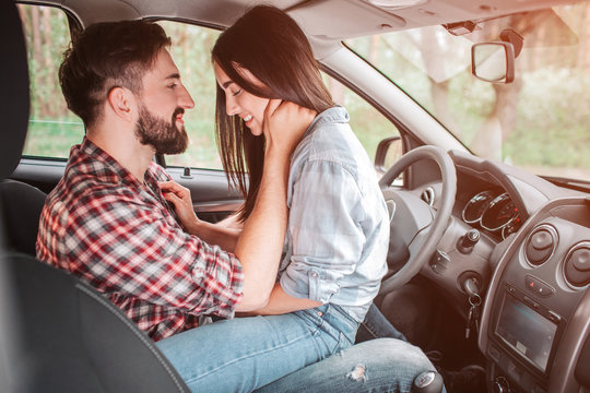 Very tender picture of young couple sitting face to face in car. He is holding his hand on her neck and looking at girl while she is holding her hands on his chest and looking down.