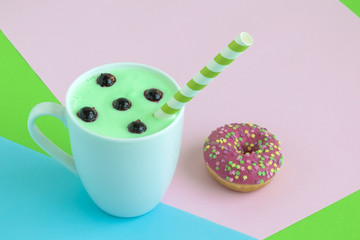 Cup of blueberries smoothie and donut on colorful background.