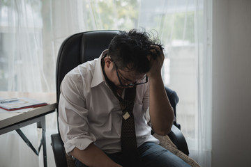 Stressed asian businessman holding his head in his hands at office desk surrounded by paperwork. feel worry ,headache ,disappoint during working