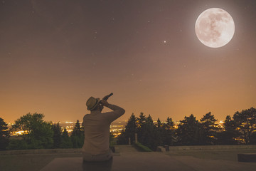 Man sitting under full moon at night with stars on the sky.