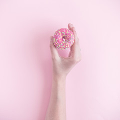 Woman hand holding small donut isolated on rose background.