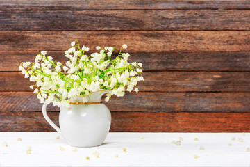 bouquet of Lily of the valley flowers in a jug on a white wooden table on a retro grunge wall background with copy space