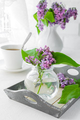 white cup with tea and a bouquet of lilac in a white vase on a summer morning breakfast at the window with a white lacy curtain in a rustic style with a copy of the space