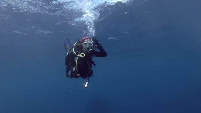Young beautiful woman scuba diver swims in blue water under surface. Bleeds air from the BCD for immersion, Indian Ocean,  Maldives
