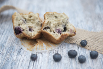 Blueberry muffin cut in half surrounded by blueberries on a wooden background 