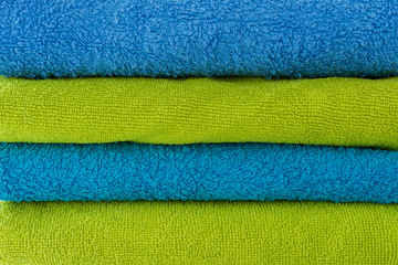 stack of clean bath-colored multicolored towels for the bathroom and a basket with towels twisted against a light background