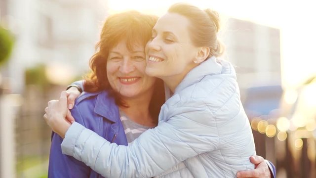 A mature mother and an adult daughter met on the street and embrace. Happy family, continuity of generations. Mothers Day