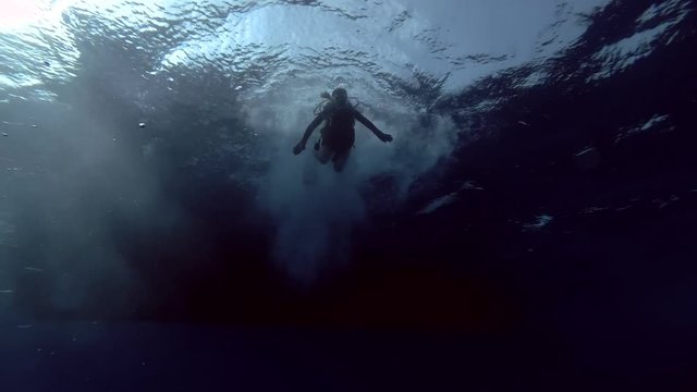Female scuba diver jumps into the water with a diving boat (underwater view), Indian Ocean,  Maldives
