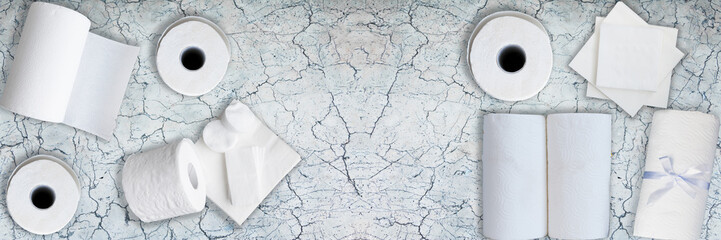 Paper tissue, white toilet  paper rolls, towels, napkins, cotton pads stacked on old gray marble table. Top view. Copy space. Wide panoramic image.