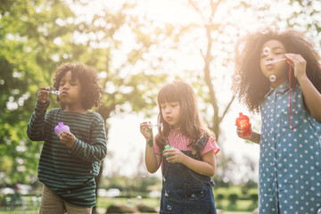 Obraz premium Group of Diverse Kids cute friends having bubble fun on green lawn in park