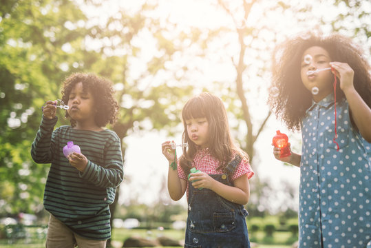 Group Of Diverse Kids Cute Friends Having Bubble Fun On Green Lawn In Park