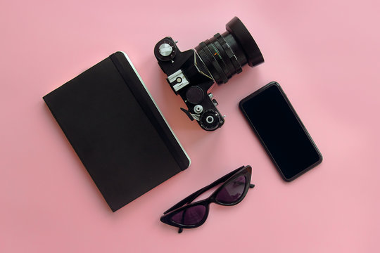 stylish black sunglasses,smartphone,photo camera and notebook on pink background, flat lay. modern hipster image. instagram blogging. space for text. summer vacation