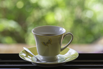 Black coffee in a cup placed at a wooden window in the morning.