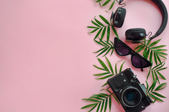 stylish black photo camera with green palm leaves, sunglasses and headphones on trendy pink background, flat lay. modern hipster travel  image. summer vacation, space for text