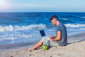 Young man sitting on beach with laptop