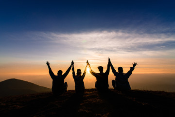 silhouette of friends shake hands up and sitting together in sunset for happiness,business...