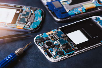 The inside of the smartphone's motherboard and tools lay on the back table. the concept of computer...