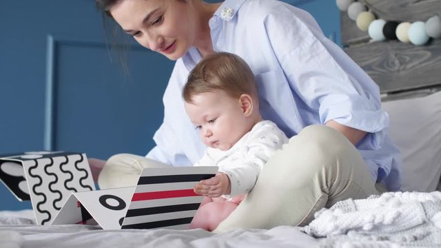 Young mother and baby watching a picture book at bedroom