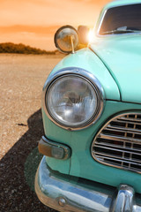 Headlight of a vintage classic old car in the autumn golden sky at sunset time.
