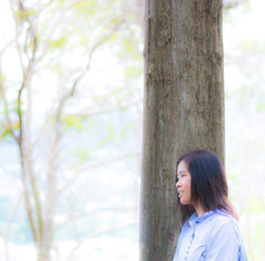 Woman is standing close to the tree feel relax by her eys that look forward in the garden with blur and soft background