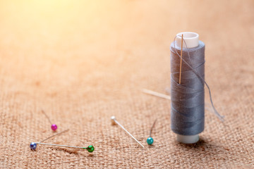 Coil thread with a needle stuck in it next to the tailor pins on the burlap, tinted light