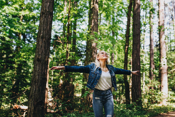 Young blond woman enjoying the nature, outstretched arms while enjoying the fresh air in green forest