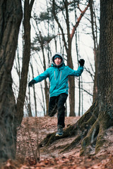 Naklejka premium Young man running outdoors during workout in a forest among leafless trees on cold freeze autumn day