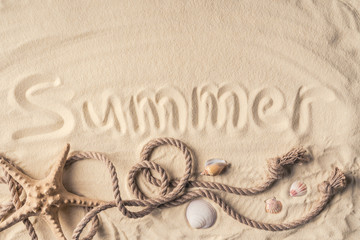 Starfish and shells with rope on light sand with summer inscription
