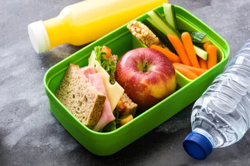 Poster Healthy school lunch box: Sandwich, vegetables ,fruit and juice on black stone © chandlervid85