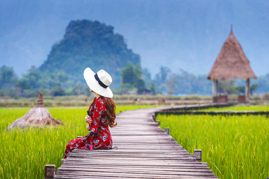 Young woman sitting on wooden path with green rice field in Vang Vieng, Laos.