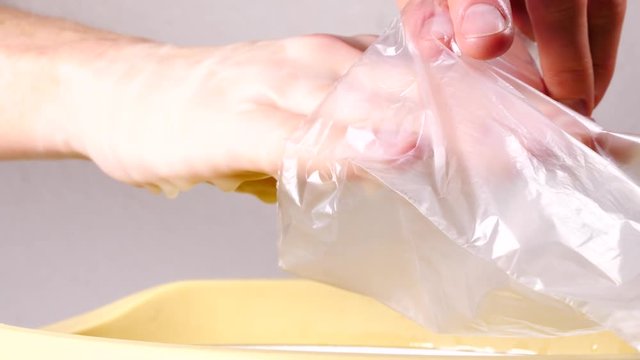 Close up slow motion shot of unrecognizable woman putting hand in plastic bag after paraffin bath taking care of hands skin.