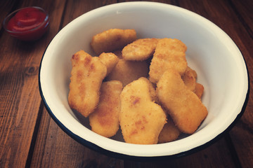 Appetizing, bright and beautiful chicken nuggets in an iron bowl and tomato sauce in the background