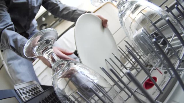 Man taking out the dishes from a dishwasher and looking at how clean they are.