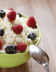 Cottage cheese in green bowl with raspberries and blueberries on wooden background. Healthy Breakfast. Good for diet.