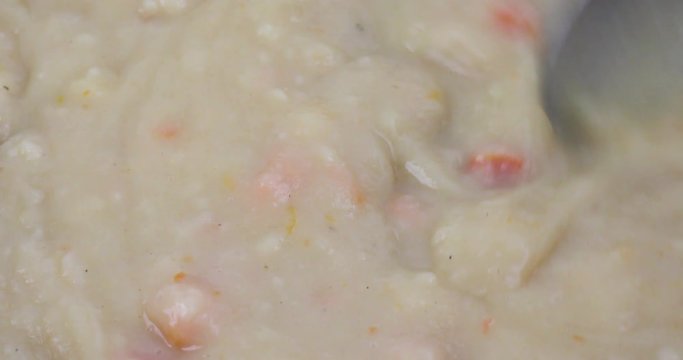 Very close video of stirring hot potato soup in a pan with a spoon.