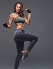 Smiling fitness brunette woman in a gray sportswear posing in a studio.