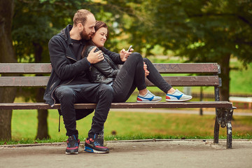 Attractive modern couple sitting on a bench in a park.