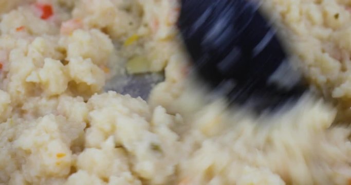 Very close video of stirring canned potato soup in a pan with a black spoon while heating.