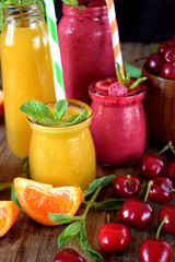 Yellow and red smoothies in glass jars surrounded by mandarins and cherries