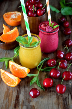 Yellow and red smoothies in glass jars surrounded by mandarins and cherries